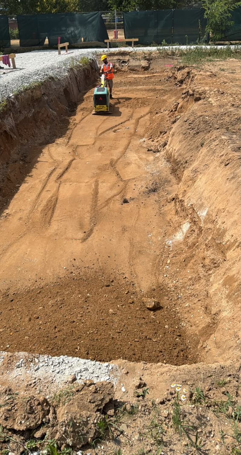 Mitarbeiter verdichtet die Sohle einer Baugrube mit einer Rüttelplatte