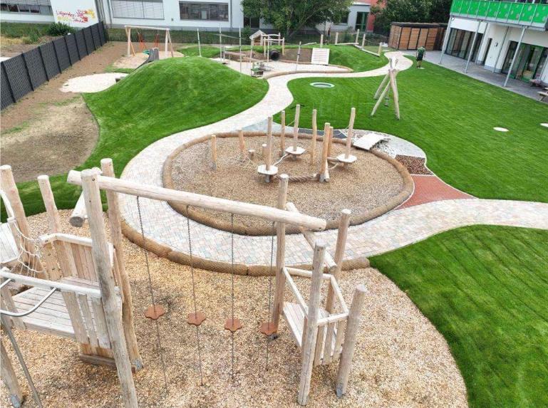 Außenanlage mit Spielgeräten, Pflasterweg und Rasen
